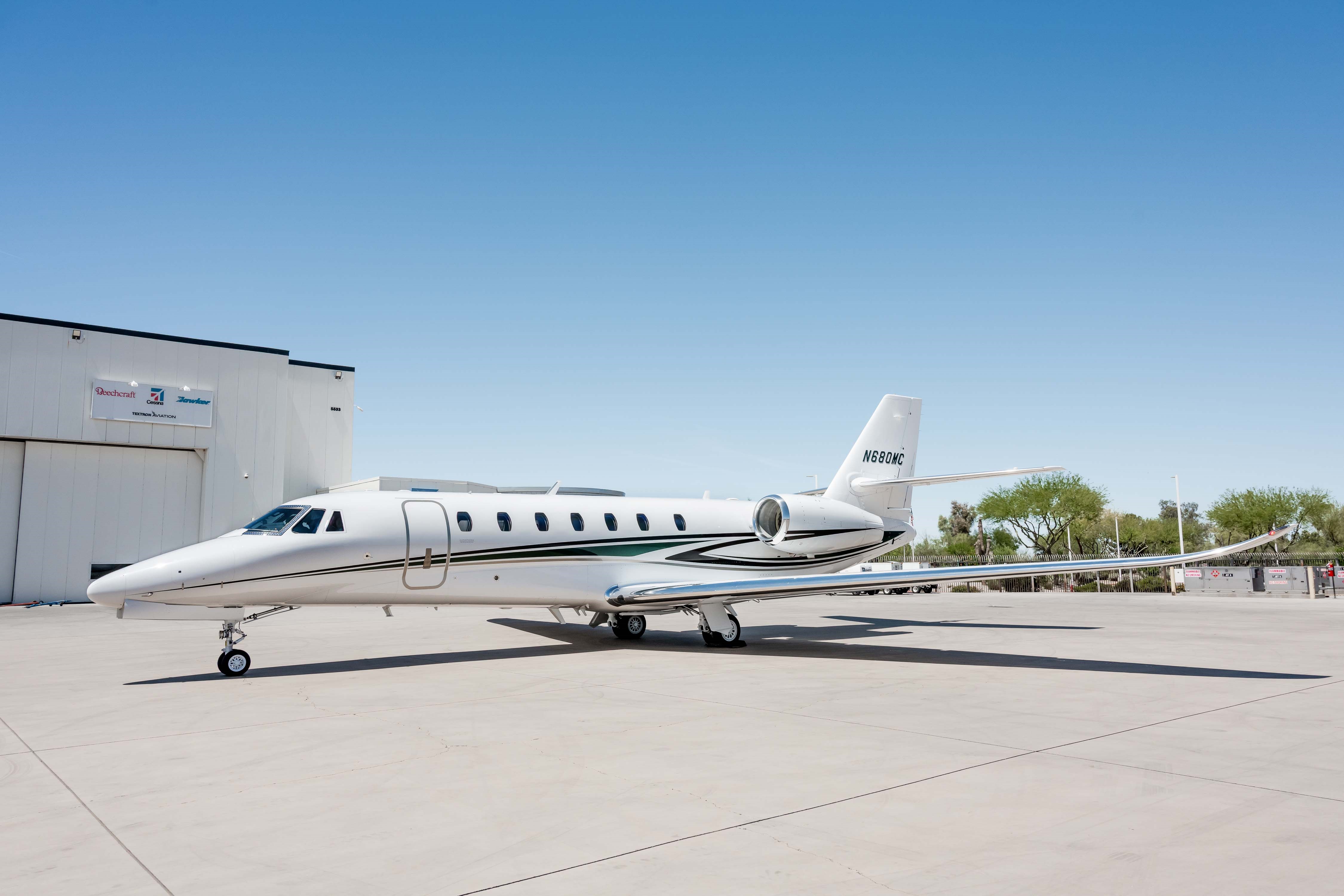 A side view of a white Cessna Citation Latitude business jet, registration N680MC, parked on a tarmac next to a hangar.